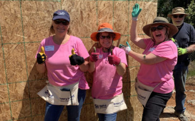 Smiling volunteers posing with thumbs up in front of a building in progress.