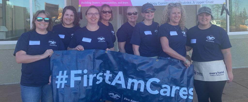 A group of volunteers in dark blue shirts, holding a sign that says, "#FirstAmCares."