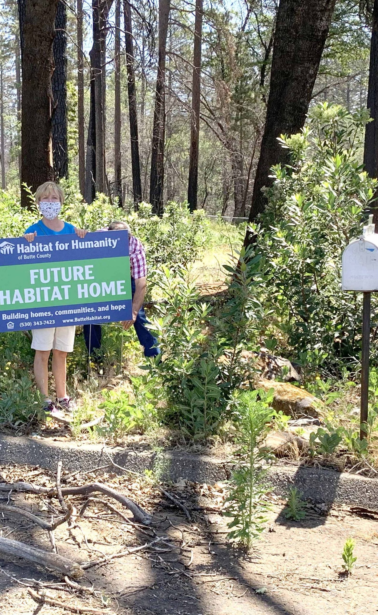 A person standing on an empty lot with a sign that says, "Future Habitat Home."