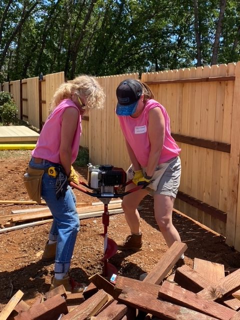 Two women using a large drill to make a hole in the ground.